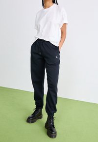 Weißes Baumwoll-T-Shirt kombiniert mit dunkelblauen Jogginghosen mit Kordelzug am Bund und Seitentaschen. Schwarze Schnürstiefel im Combat-Stil vervollständigen den Look.