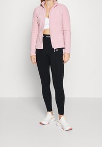 Light pink fleece jacket with a high collar, paired with black leggings and white athletic shoes featuring yellow and pink accents.
