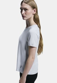 Vit kortärmad träningsskjorta med rundad halsringning. Tillverkad av en slät tyg, med en logotyp på vänster nedre sida.