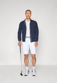 Navy zip-up jacket, white polo shirt, white shorts, black golf club, and athletic shoes. Smooth textures and contrasting colors.