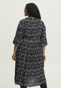 Maximeikka, jossa on tummia kukkakuoseja sinisenä ja valkoisena mustalla taustalla, rypytetty pääntiellä ja kolmivartaloisilla kellohihansuilla.