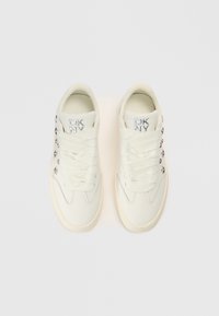 Λευκά αθλητικά παπούτσια με λείο δερμάτινο επάνω μέρος, υφασμένα κορδόνια, ασημί σήμανση και διακοσμητικά καρφιά στο πλάι. Στρογγυλεμένη σχεδίαση μύτης.