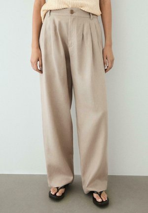 Beige højtaljede brede bukser med folder, båret med sorte platforme-flipflops og en ærmeløs cremet striktop.