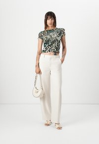 Top scurt cu imprimeu de leopard, cu mâneci strânse, asortat cu pantaloni albi cu picioare largi. Accesoriile includ o geantă mică albă și sandale.