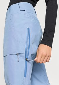 Ανοιχτό μπλε αδιάβροχα παντελόνια από Gore-Tex, με τσέπη στο πλάι που έχει φερμουάρ και κορδόνι, καθώς και ρυθμιζόμενη μέση.