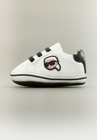 Λευκό αθλητικό παπούτσι με μαύρη σόλα και τακούνι, τρεις μαύρες λουρίδες και καρτούν πρόσωπο με γυαλιά ηλίου στο πλάι.