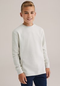 Balts garām piedurknēm krekls no teksturēta auduma ar apaļu kakla izgriezumu. Kombinēts ar tumši ziliem biksēm. Vienkāršs dizains, bez rakstiem vai akcentiem.