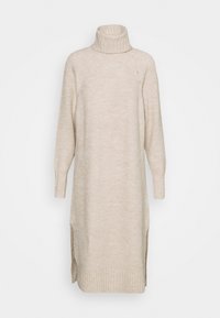 Beige neulemekko, jossa on korkea kaulus, pitkät hihat, ribbitekstuuri, sivuaukot ja suora leikkaus.