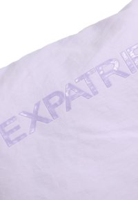 Biely textil s pokrčenou textúrou, s lesklým fialovým písmom, ktoré výrazne zobrazuje slovo "EXPATRI" na povrchu.