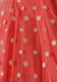Robe corail avec superposition transparente, ornée de marguerites blanches brodées. Tissu doux avec une texture délicate et des détails floraux tout au long.