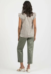 Blusenshirt mit floralem Druck und kurzen Rüschensäumen, kombiniert mit grünen Cargo-Hosen. Das Model trägt beige Block-Absatzsandalen.