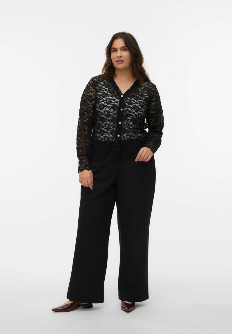 Cardigan en dentelle noire à manches longues, boutonné sur le devant avec un ourlet festonné, associé à un pantalon noir ample et des chaussures marron à bout pointu.