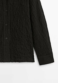 Chemise noire à manches longues avec boutons, en tissu texturé froissé avec une seule poche poitrine, vue de face et de côté.
