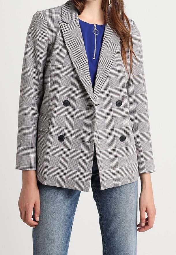 Blazer gris à carreaux croisé avec des boutons noirs, des revers crantés et des poches avant. Porté sur un haut bleu, avec un jean de couleur moyenne.