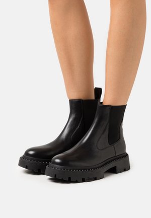 Botas de cuero negro hasta el tobillo con paneles elásticos en los laterales, suela de goma gruesa y detalles texturizados. Diseñadas para un uso fácil y estabilidad.