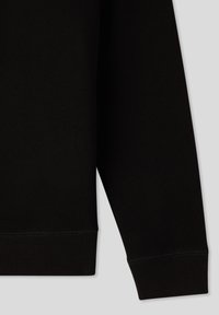 Felpa nera con polsini a coste, caratterizzata da una texture di tessuto liscia e un design semplice. La manica si estende al di fuori dell'inquadratura.