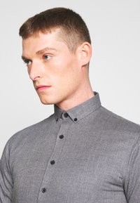 Camicia grigia con bottoni in tessuto testurizzato, dotata di colletto classico e bottoni neri. Design aderente.