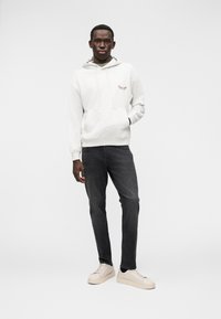 Γκρι φούτερ με κουκούλα, μπροστινή τσέπη και λογότυπο, σκούρο τζιν και ανοιχτόχρωμα αθλητικά παπούτσια. Απλός σχεδιασμός, απαλή υφή, άνετη εφαρμογή και διακριτική παλέτα χρωμάτων.