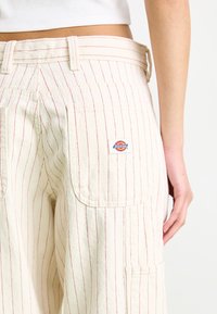 Cream cargo pants with red vertical stripes, featuring side pockets and a small Dickies logo tag on the back pocket.