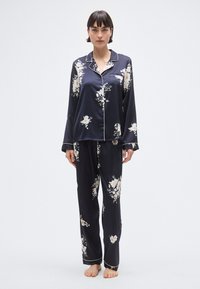 Ensemble de pyjama en satin bleu marine avec imprimé floral. Le haut à manches longues présente un col et des bordures contrastées ; pantalon assorti avec ceinture élastique.