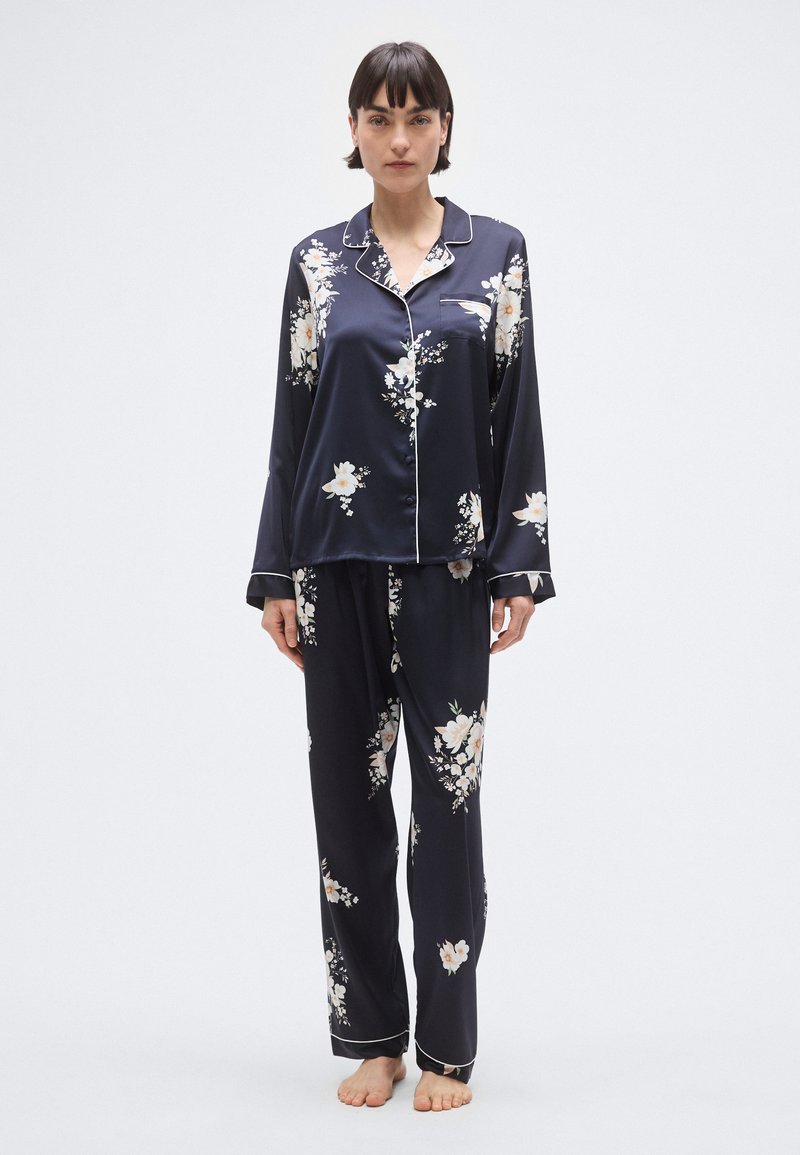 Ensemble de pyjama en satin bleu marine avec imprimé floral. Le haut à manches longues présente un col et des bordures contrastées ; pantalon assorti avec ceinture élastique.