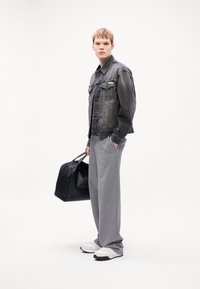Denim jacket in faded gray with button-up front and chest pockets; gray sweatpants; black duffel bag; white sneakers. Simple, modern design.