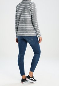 Grårandig långärmad skjorta kombinerad med mörkblå slim fit jeans och svarta sneakers. Har en rund hals och skräddarsydd passform.