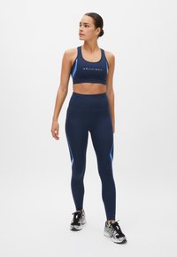 Conjunto deportivo navy que incluye un sujetador deportivo ajustado con acentos azules contrastantes y leggings de cintura alta con detalles en los paneles laterales, fabricados en material elástico.