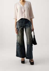 Blouse rose clair à col en V et manches trois-quarts, associée à un jean en denim large et déchiré avec poches cargo et accents décolorés.