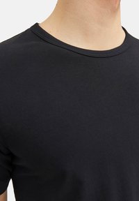 Nahaufnahme einer Person, die ein schlichtes schwarzes Rundhals-T-Shirt trägt, wobei der Ausschnitt und der obere Brustbereich zu sehen sind.