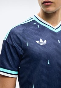 Mann som har på seg en mørkeblå Adidas sportstrøye med lyseblå striper på skuldrene og små, spredte lyseblå diamantmønstre.