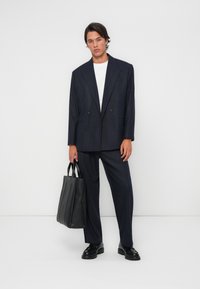 Costume à rayures marines avec un blazer croisé et un pantalon droit, associé à un t-shirt blanc et un sac fourre-tout noir.