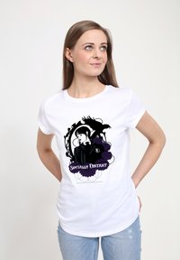 Mladá žena v bílém tričku s černým a fialovým gotickým designem dívky, havrana, květin a nápisu "Sociálně vzdáleni", oblečená v modrých džínách.