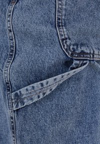 Denim fabric, light blue color, with visible stitching. Features a folded pocket detail at the seam, displaying texture and pattern variations.