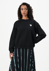 Black sweatshirt made of cotton, featuring a white flower design on the chest, paired with a pleated black skirt with blue stripes.