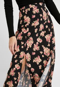 Jupe fleurie en tissu noir avec des fleurs roses, dotée d'une fente haute et d'une taille cintrée. Texture lisse avec un design fluide.