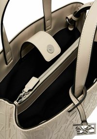 Borsa a mano in pelle beige con interno nero, chiusura con zip superiore, patta con chiusura a scatto e ciondolo con logo. Presenta un design strutturato e cuciture a contrasto.