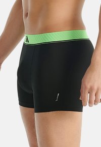 Svarta boxershorts med en bred, strukturerad grön midja, med en tunn svart dekorlinje och en liten logotyp p å benet.