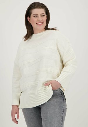 Pull en tricot blanc avec des rayures texturées, des poignets côtelés et un ourlet arrondi. Associé à un jean gris, mettant en avant une coupe décontractée et un style casual.