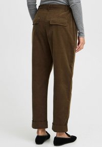 Brown, relaxed-fit trousers with rolled cuffs and two back pockets. The material appears textured, with a subtle fabric weave.