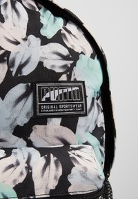 Sac à dos à motif floral noir, gris et bleu clair avec un patch logo Puma rectangulaire cousu sur la poche avant.