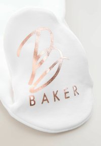 Biały materiał o gładkiej fakturze z różowo-złotym metalicznym logo stylizowanym jako "B BAKER" w pogrubionym kroju pisma.