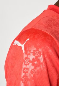 Rød atletisk trøje med struktureret stof, et subtilt mønster og et hvidt Puma-logo på skulderen.