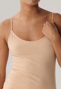 Nago bezrękawnik wykonany z gładkiego materiału, z cienkimi ramiączkami i okrągłym dekoltem. Materiał jest miękki i lekko elastyczny.
