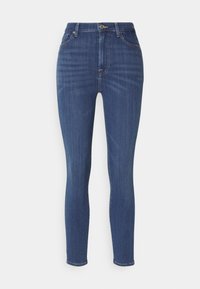 Jean skinny en denim bleu foncé. Design taille haute avec cinq poches, quincaillerie dorée et détails de couture subtils le long des coutures.