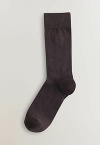 Calzino marrone scuro a metà polpaccio con bordo a coste e piccolo logo ricamato "N" vicino alla parte superiore su uno sfondo chiaro.