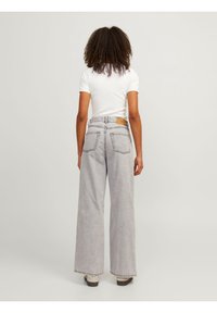 Grå jeans med vida ben och hög midja, med bakfickor och kontrasterande sömmar. Matchas med en enkel vit skjorta.