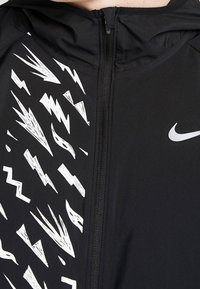 Zwarte sportieve jas met een rits aan de voorkant en een capuchon, met gedurfde witte bliksemflitspatronen aan één kant en een klein logo.