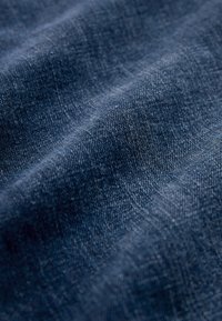 Detailný záber textúrovaného tmavomodrého džínsového materiálu s viditeľným vzorom tkania a jemnými svetelnými odleskami.