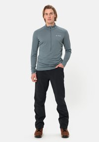 Ljusblå långärmad zip-up topp och svarta byxor, kombinerad med bruna vandringskängor. Tyget ser slätt ut med en figursydd design.